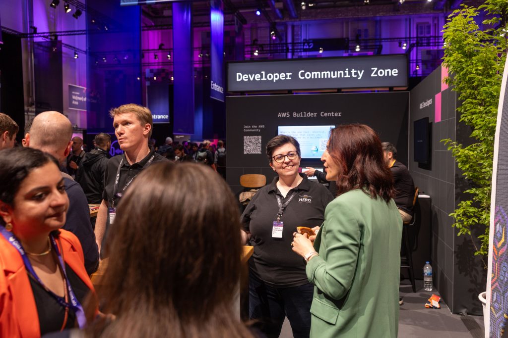 Die Developer Community Zone mit Teilnehmenden an Stehtischen, Community-Bannern und einer Bühne im Hintergrund.