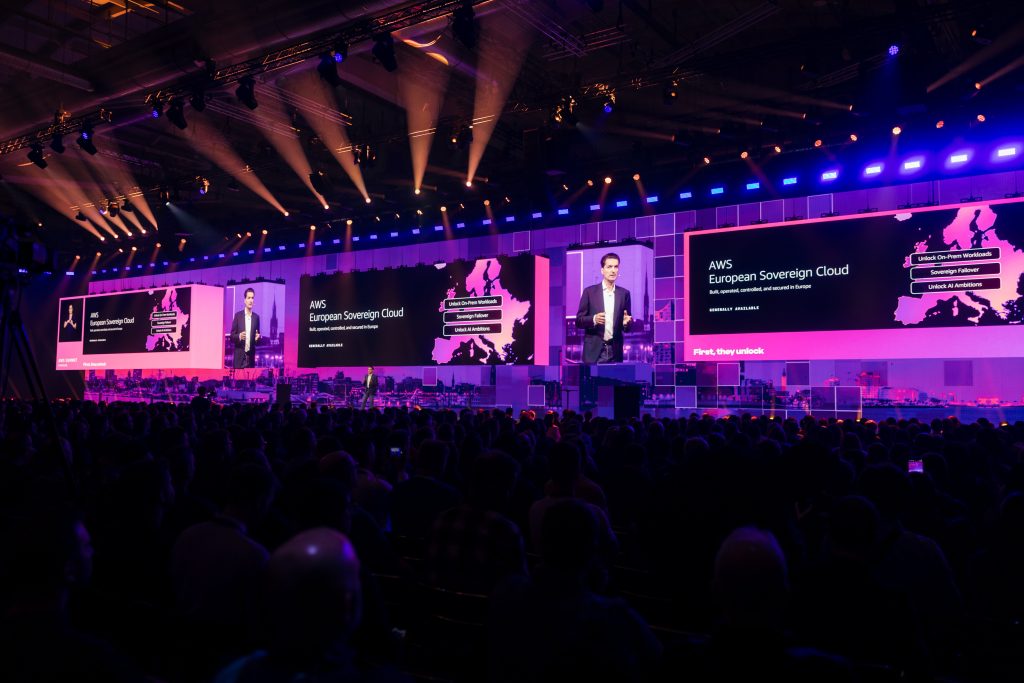 Stefan Höchbauer auf der Keynote-Bühne des AWS Summit Hamburg 2026 vor einem großen Publikum in einer abgedunkelten Messehalle.