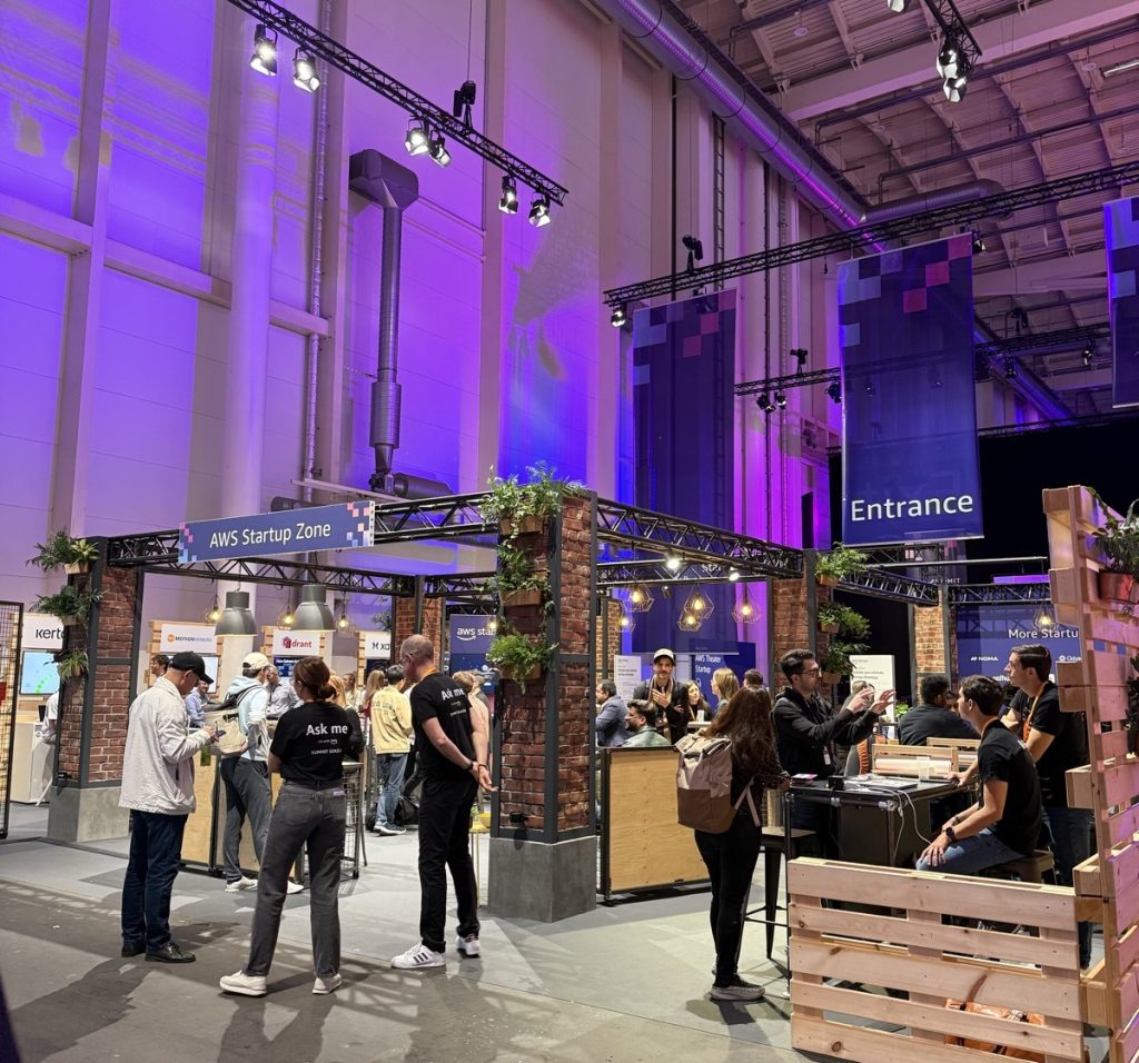 Die Startup Zone mit Backsteinpfeilern, Holzpaletten und Pendelleuchten – Startups präsentieren ihre Lösungen in einer Lounge-Atmosphäre.