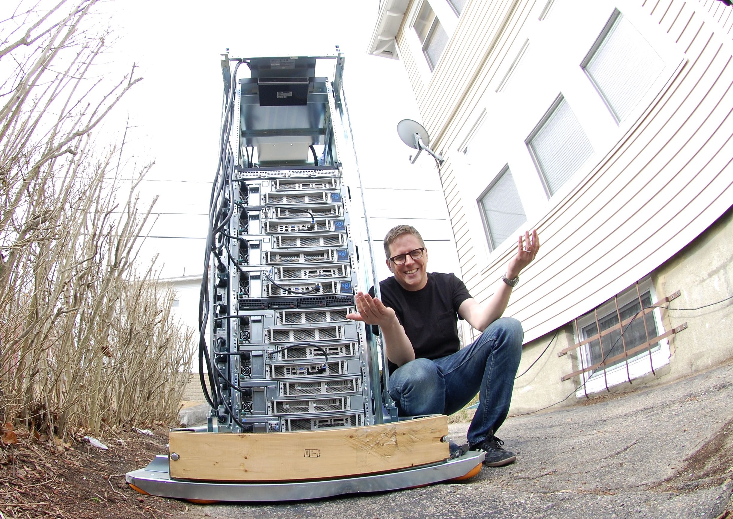 Image of Chris Dagdigian squatting next to a rack of servers, with his hands outstretched in a questioning pose