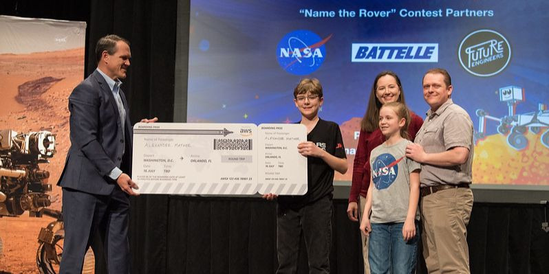 Jaime Baker (left), from Amazon Web Services (AWS), presents a ticket to Cape Canaveral to the Name the Mars Rover 2020 contest winner Alex Maver and his family.