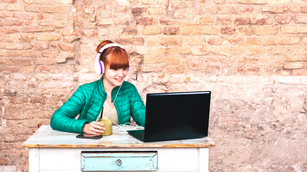 woman sitting at table with headphones and laptop