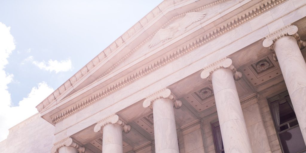 exterior shot of government building with columns, looking up sun behind