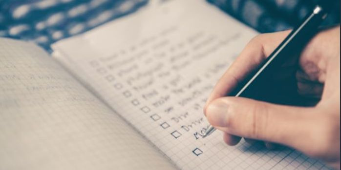 close up of hand with pen writing checklist in notebook