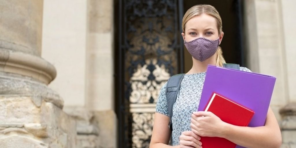 female student with mask holding books outside university building