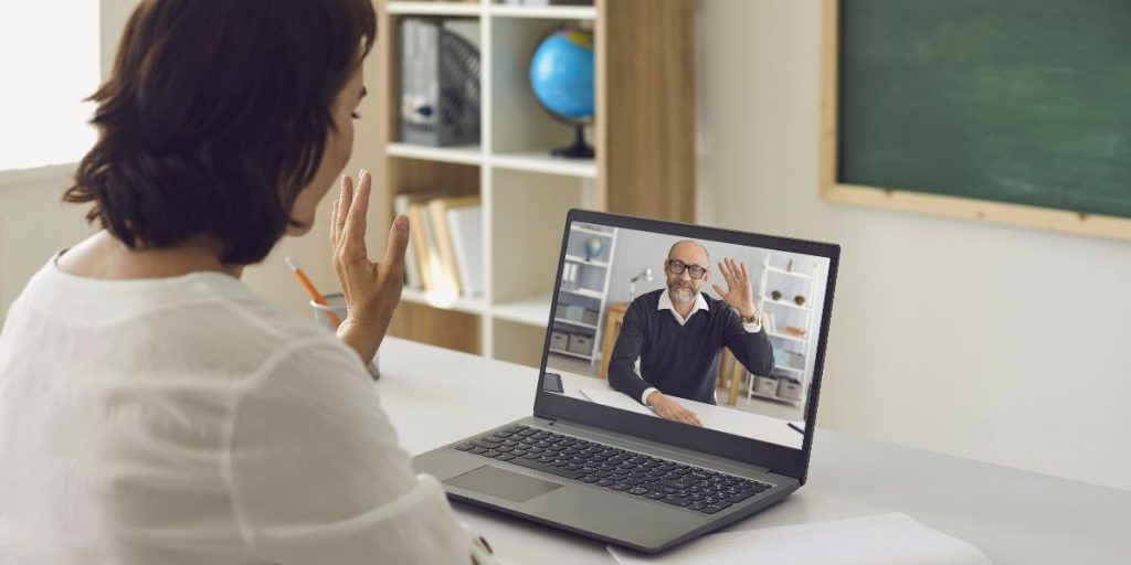 student raises hand to respond to teacher on laptop