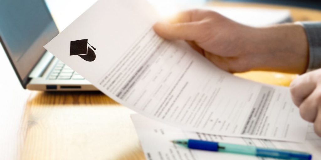 hands hold paper college application form next to an open laptop