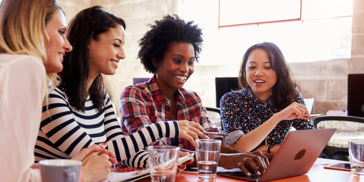 four women collaborate over a laptop