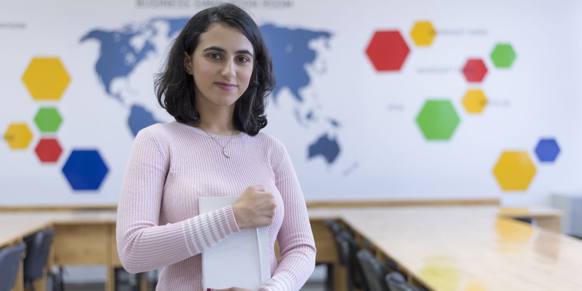 Young woman holding a notebook in front of a board in a classroom