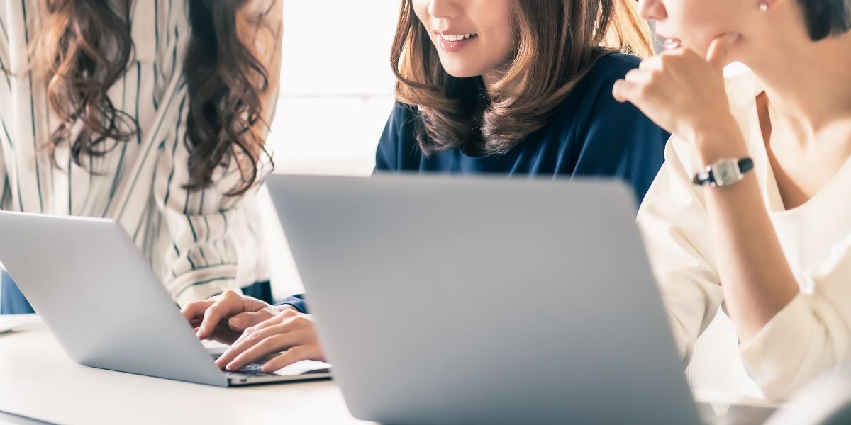 closeup of three women collaborating on laptops at office