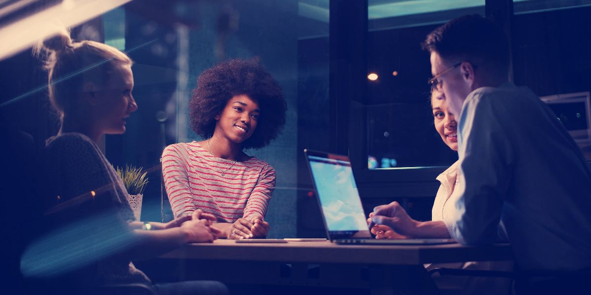 group sits collaborating at a table with a laptop