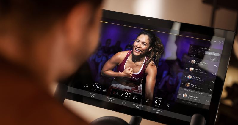 Man watching a female Peloton biking instructor through a touch screen display on his Peloton bike.