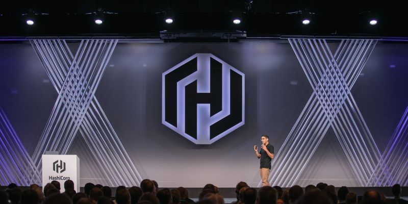 A speaker stands on stage in front of a Hashicorp logo on the display screen as an audience looks on.