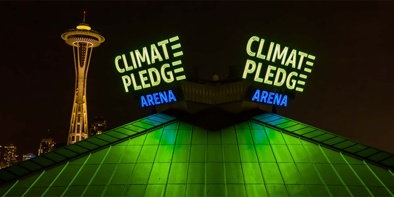 Image of sign with Space Needle over green roof with neon sign that reads Climate Pledge Arena