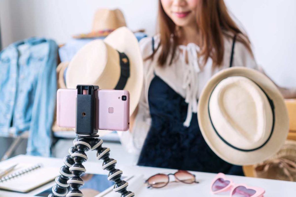 Female influencer showing off 2 different hat styles in front of phone camera