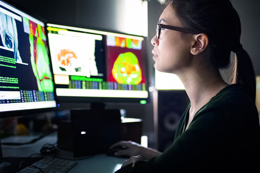 Woman in front of two computer monitors assessing her workflow