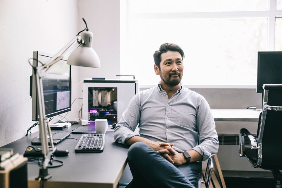 Man at desk in office with computer monitors behind him