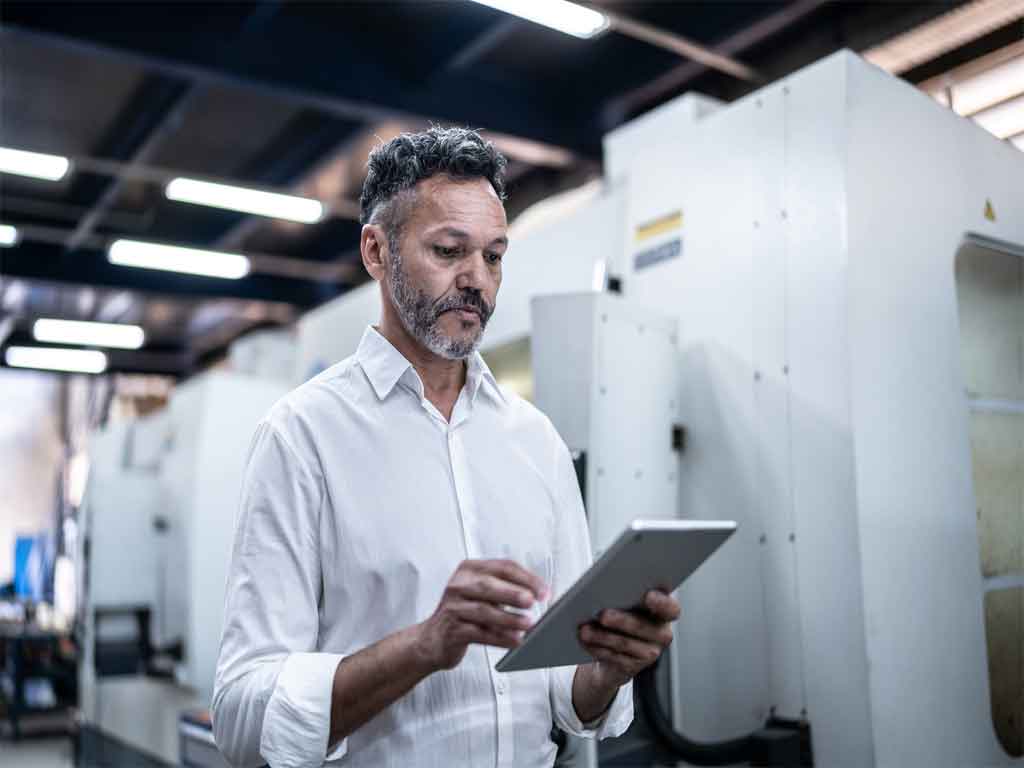 Employee standing with tablet device among heavy machinery