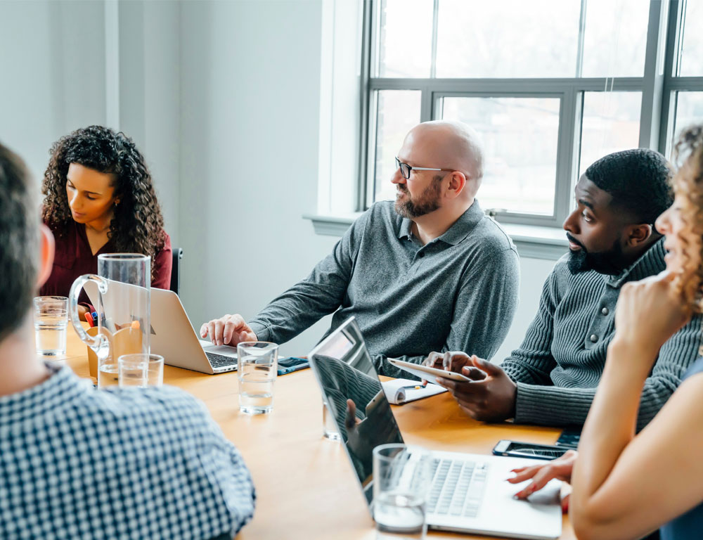 Team meeting in an office setting with three men and two women focusing on a presentation out of view