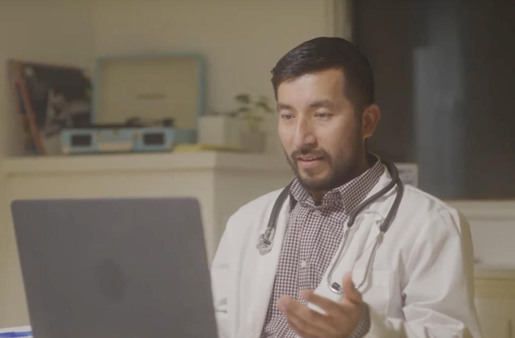 Male doctor sitting in front of a laptop chatting with a patient during a telemedicine appointment