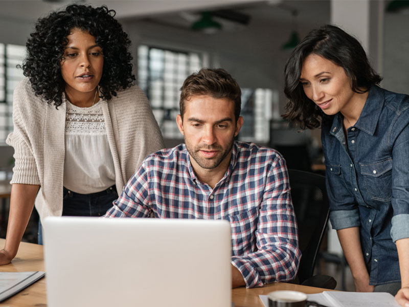 Three colleagues in an office huddling over a laptop