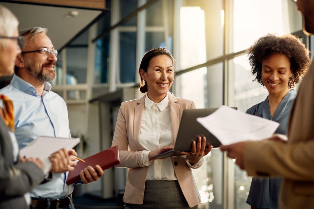 Group of coworkers standing with their papers and laptops laughing