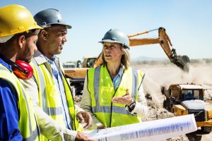 Architects and worker discussing over blueprint at quarry against clear sky