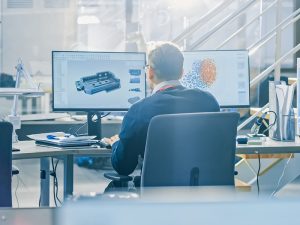 Back view of an industrial engineer working on two screens, one with CAD software and another portraying a machine learning model