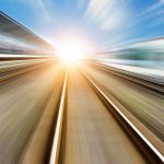 A high speed perspective image of a railway track leading into the sun on the horizon