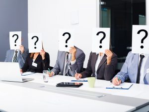 A group of business people in a meeting holding question mark signs over their faces