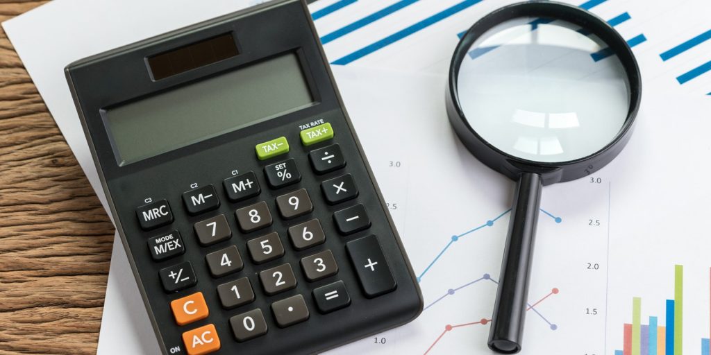 Calculator and magnifying glass on a pile of graphs and charts on a wood table