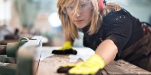 Female craftperson with protective equipment working with planks in workshop