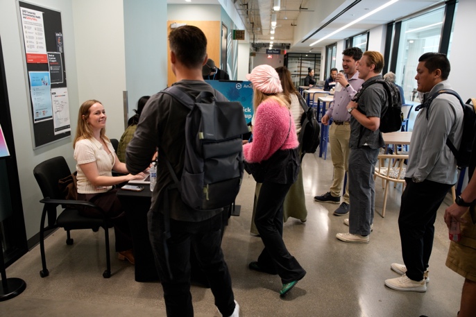 Event attendees checking in and networking in a modern building corridor during the Amazon Quick User Group meetup in Los Angeles. A registration table is visible on the left with small groups of people conversing casually.