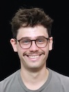 Professional headshot of a young man wearing glasses and a gray shirt against a black background