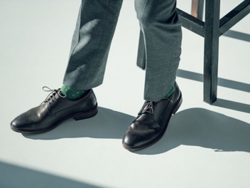 Close-up product photograph of polished black leather oxford dress shoes worn with gray business trousers in professional setting with natural lighting and minimal background