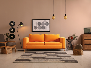 3D rendered modern living room interior design with vibrant orange sofa as focal point, moon phase wall art, brass pendant lights, mid-century furniture, and warm beige color scheme