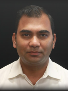 Professional headshot of a man with short dark hair and facial stubble wearing a white collared shirt against a dark background