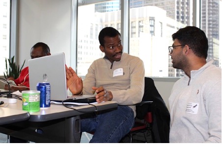Two attendees discussing a workflow at a table, one explaining while the other listens