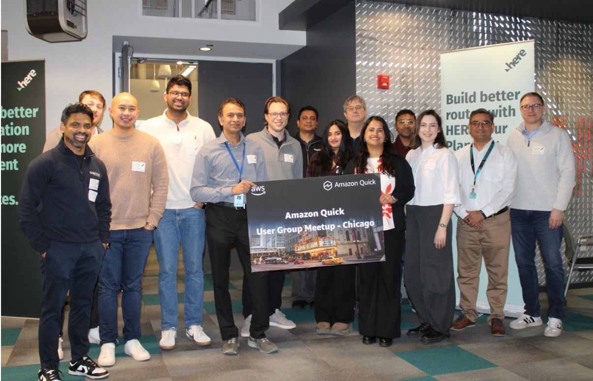 Organizers and speakers holding an Amazon Quick User Group Chicago sign, with HERE Technologies banners behind them